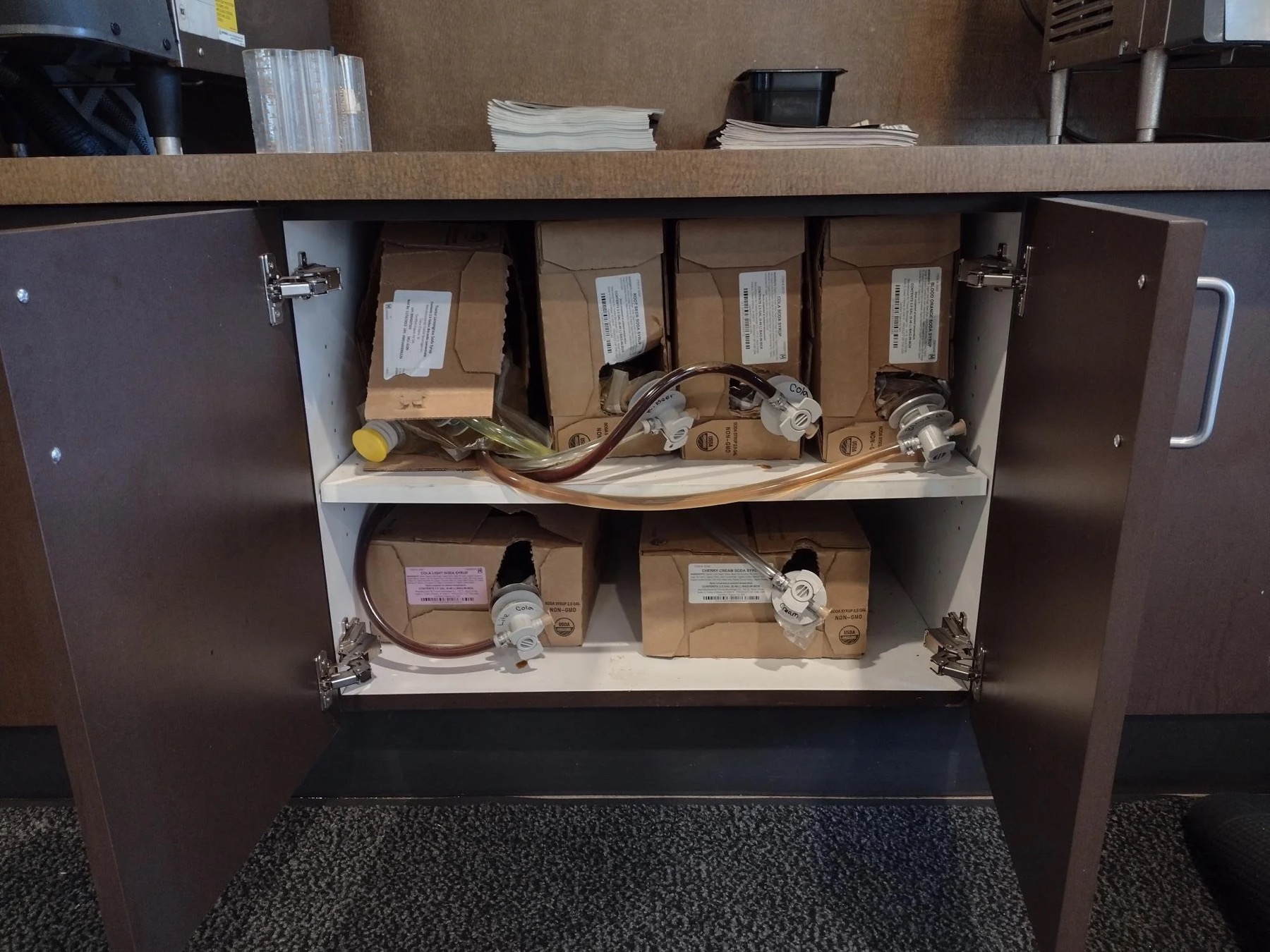 Syrup boxes and beverage lines inside the Saladworks counter cabinet